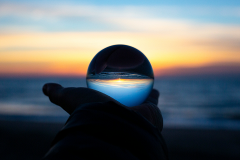 A photo of a hand holding a crystal ball containing the sky and a body of water.